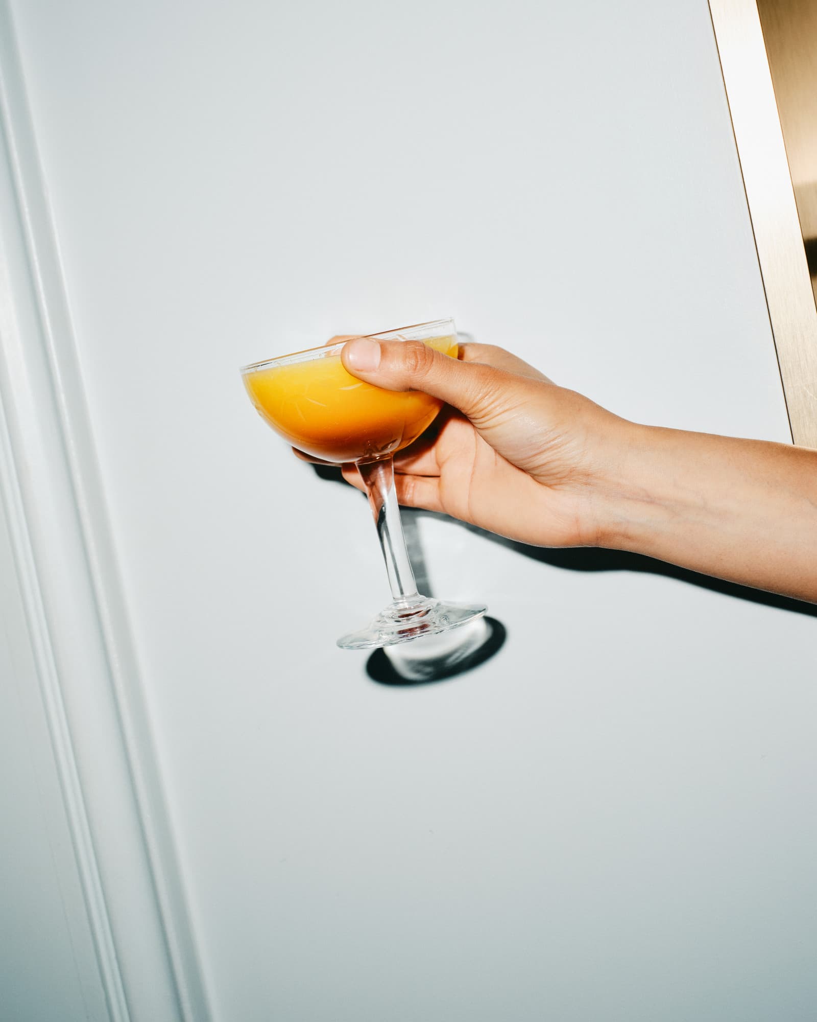 hand holding a coupe of cloudy orange wine against a white door, flash